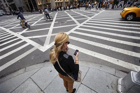 A woman uses her Apple iPhone while waiting to cross 5th Avenue in New York